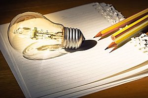 a shining lightbulb and pencils on top of lined paper symbolizing the creation of content for law firms which is a good content marketing strategy