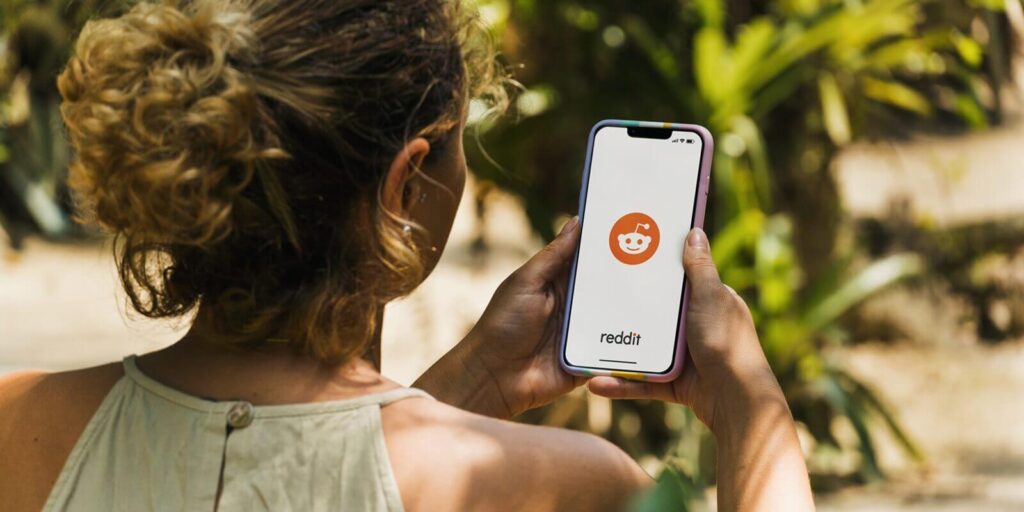 girl in the park holding a smartphone with Reddit social media app on the screen