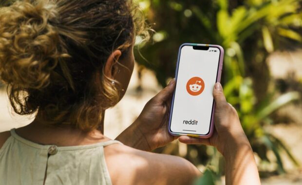 girl in the park holding a smartphone with Reddit social media app on the screen